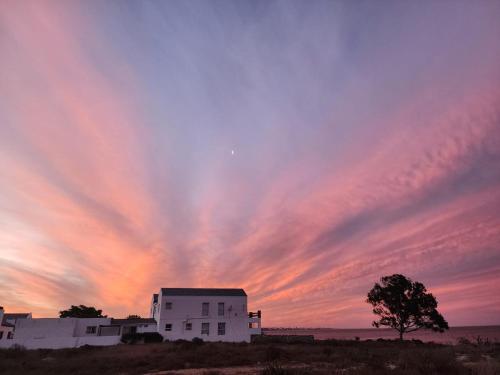 a sunset over a white building with a tree at 23 On Beach in Stompneusbaai