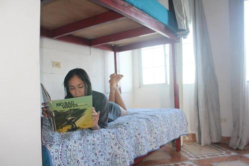 a woman sitting on a bed reading a book at Hotel Palmar Surf Camp & School in San Carlos