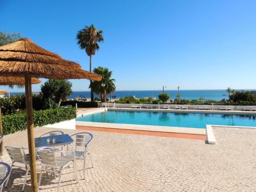 a pool with a table and chairs and a straw umbrella at Almar Hotel Apartamento in Albufeira