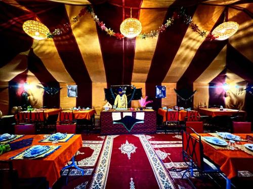 a dining room with red tables and chairs and a chef at ibis merzouga camp in Merdani
