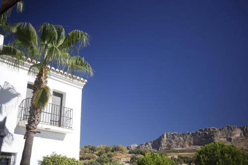 a white building with a palm tree and mountains in the background at La Posada del Torcal in Villanueva de la Concepción
