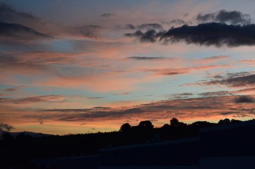 a sunset with trees and clouds in the sky at Kakaw's house, pool with a view of the 3 volcanoes in San Juan Alotenango