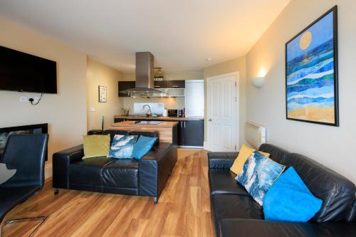 a living room with a black leather couch and a kitchen at two bed Seafront apartment - sea views in Aberystwyth