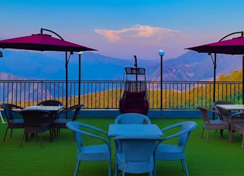 a balcony with tables and chairs with a view of mountains at The Pine Woods A Luxury Resort in Mussoorie Rooftop Restro in Mussoorie