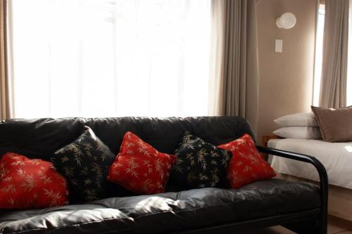 a black leather couch with red and black pillows at Ondini Guest House in Winterton