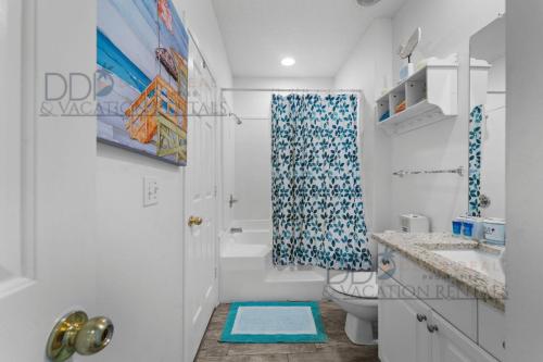 Baño blanco con cortina de ducha azul y aseo en Legacy Villa 1503, en Gulfport