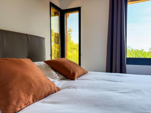 a bed with brown pillows in a room with windows at CAP PARADISU - Chalet vue mer et montagne in Santa-Maria-di-Lota