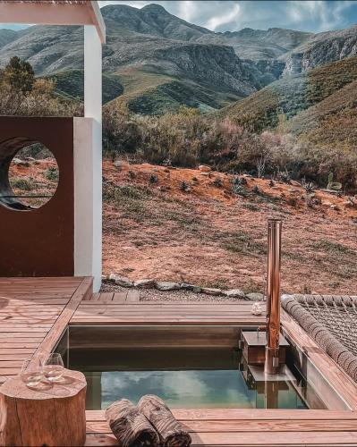a pool of water with a wooden deck and mountains at White Stone Retreat in Oudtshoorn