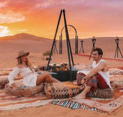 a man and a woman sitting on large tires in the desert at Eternal Luxury Camp in Merzouga