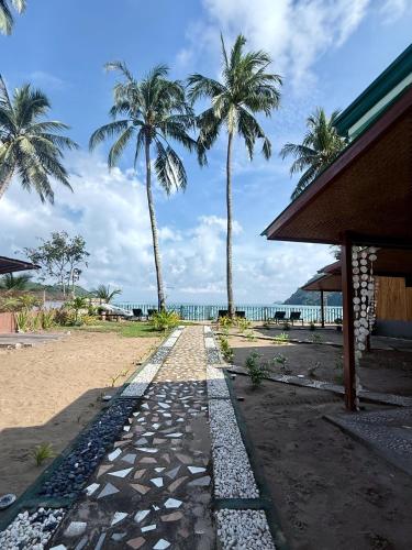 a walkway on the beach with palm trees and the ocean at Kattegat Beachfront Villa in El Nido