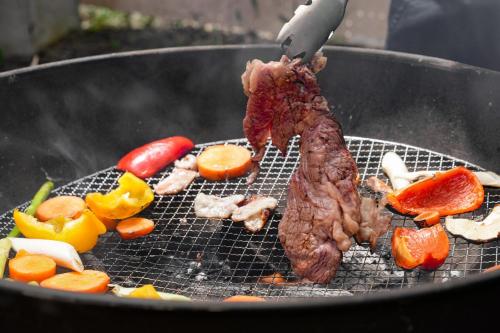 a piece of meat cooking on a grill with vegetables at アウトドアアドベンチャー北軽井沢 in Wada