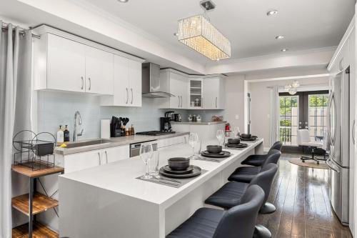a white kitchen with a large white island with chairs at Entire Unit - Steps From History - 5 Mins To Beaches in Toronto