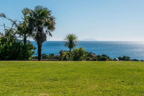 a green field with palm trees and the ocean at Cypress Ridge Estate - Stay Waiheke in Onetangi