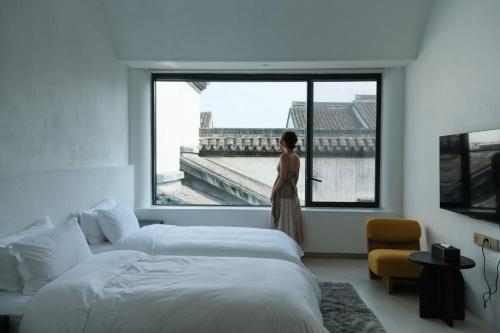 une femme debout dans une chambre donnant par la fenêtre dans l'établissement 江南赋园林私汤设计师民宿, à Guanqiaocun