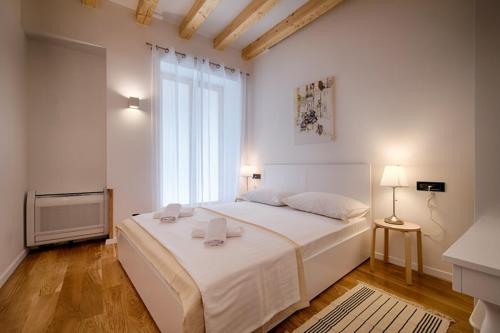 a white bedroom with a large bed and a window at Apartments Villa Glorija in Komiža