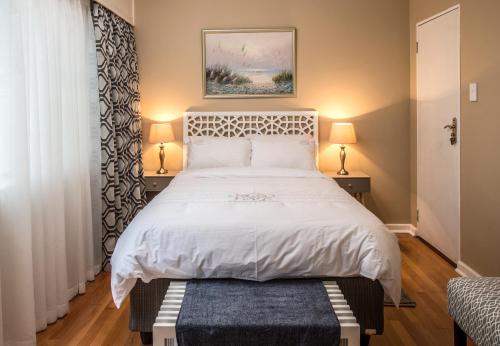 a bedroom with a large white bed with two lamps at Bhotani Lodge in Port Elizabeth