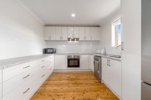 a kitchen with white cabinets and a wooden floor at Blissful Blayney Home - Comfy Cosy and Sleeps 6 in Blayney