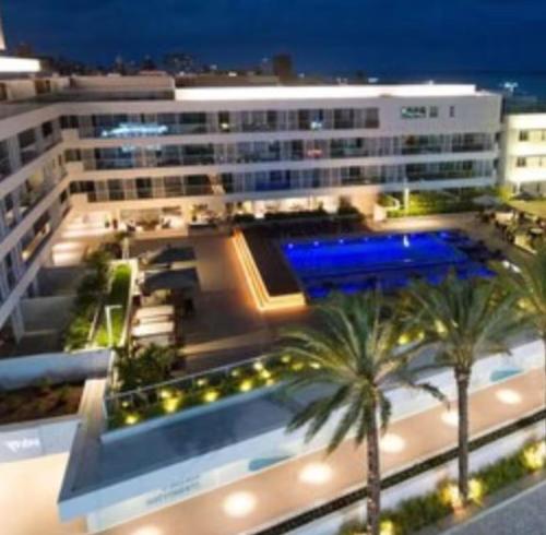 a large building with a swimming pool and palm trees at Loft Alto padrão na beira mar de Tambaú in João Pessoa