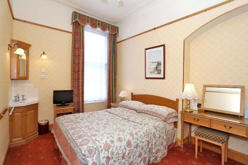 Habitación de hotel con cama, escritorio y TV. en Butlers Guest House, en Aberdeen