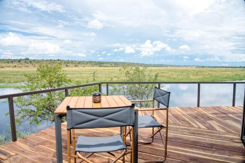 a table and two chairs on a wooden deck with water at Chobe River Camp in Ngoma