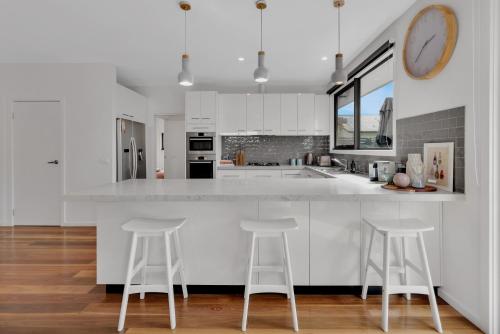 a kitchen with white cabinets and white counter stools at Bridge Beach House Central Barwon Heads Sleeps 12 Walk everywhere Accessible lower level bedroom and bathroom in Barwon Heads