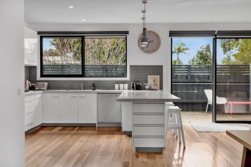 a kitchen with white cabinets and a large window at Bridge Beach House Central Barwon Heads Sleeps 12 Walk everywhere Accessible lower level bedroom and bathroom in Barwon Heads