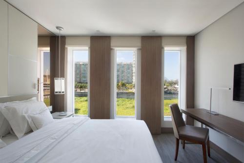 um quarto com uma cama, uma secretária e janelas em Venit Barra Hotel no Rio de Janeiro