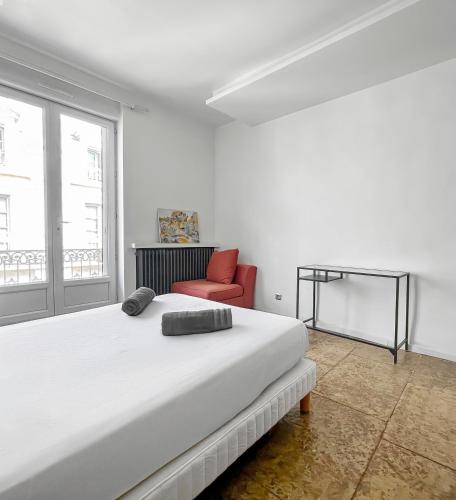 a white bedroom with a bed and a red chair at Le Balcon de la Comédie in Montpellier