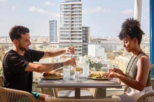 a man and woman sitting at a table eating food at Novotel Malta Sliema in Il-Gżira