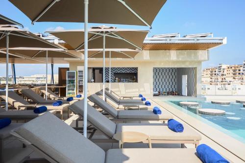 a swimming pool with lounge chairs and umbrellas at Novotel Malta Sliema in Il-Gżira