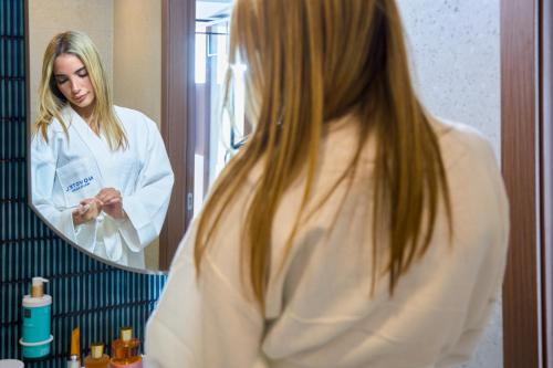 a woman looking at her reflection in a bathroom mirror at Novotel Malta Sliema in Il-Gżira