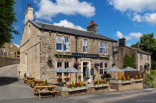 an old stone building with benches and umbrellas in front at The Craven Heifer in Addingham