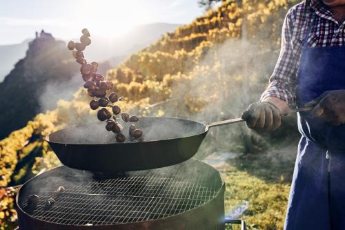 a man cooking food in a pan on a grill at Hotel Tyrol in Malles Venosta