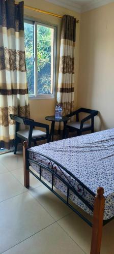 a bedroom with a bed and two tables and a window at Cozy Guest Room in Kinshasa with Balcony and Partial Air-Conditioning in Lemba-Gaba
