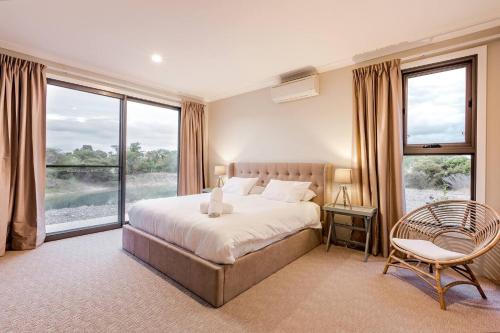 a bedroom with a bed and a chair and windows at Bonnie and Piper - Lakeside and Wine Country Living in Wilyabrup