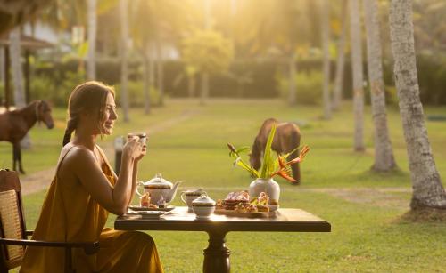 a woman sitting at a table with a cup of coffee at Tamarind Tree Garden Resort - Katunayake in Negombo