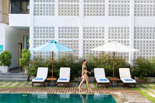 a woman walking by a pool in front of a building at ÊMM Hotel Hoi An in Hoi An