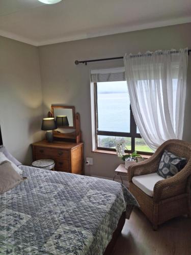 a bedroom with a bed and a window and a chair at Notre Petit Paradis in Mossel Bay