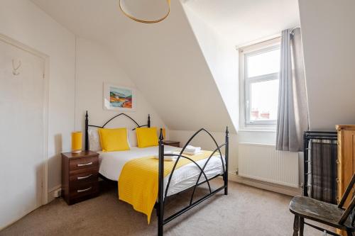 ein Schlafzimmer mit einem Bett mit gelben Kissen und einem Fenster in der Unterkunft Victorian Cartref in the heart of Llandudno in Llandudno