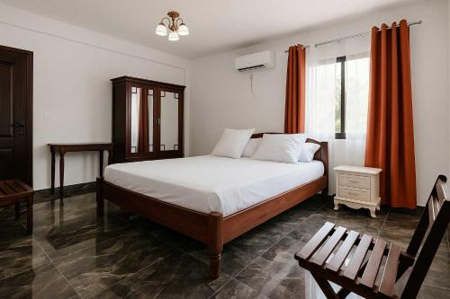 a bedroom with a bed with white sheets and orange curtains at Appart Nouvelle Ville Toamasina in Toamasina