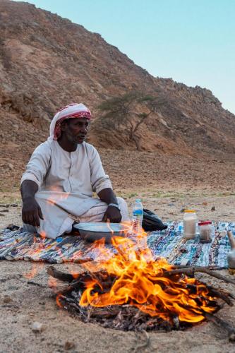 a man sitting next to a camp fire at Marsa Shagra Village in Abu Dabab
