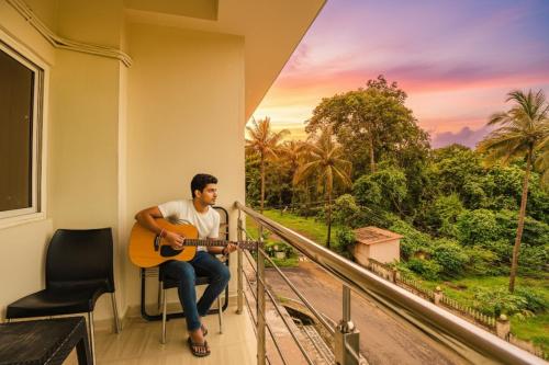 a man sitting in a chair playing a guitar on a balcony at FabHotel Prime Swarnam, Old Goa in Old Goa