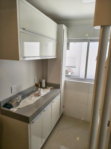 a small kitchen with white cabinets and a window at Apartamento aconchegante com ar, secadora e adega in Piratuba