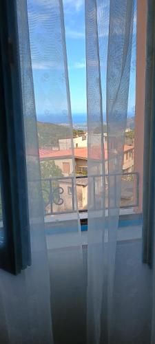 a window with white curtains and a view of a building at Sa Omu 'Eccia in Villagrande Strisaili