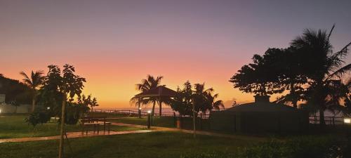 a sunset over a beach with a tent and palm trees at Spacieux haut de villa proche plage in Anse-Bertrand