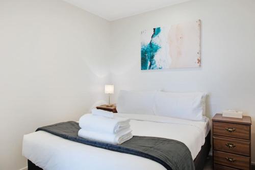 a bedroom with a bed with white sheets and a nightstand at City Vista Apt with Views - Pool and Gym in Auckland