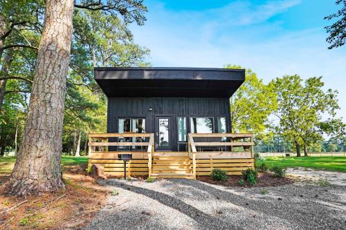 a tiny house with a black roof next to a tree at Waterfront 1BR on Working Farm with Deck and View in Hacksneck