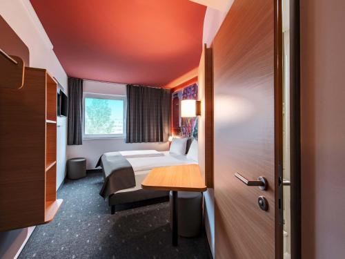 a hotel room with a bed and a desk and a door at B&B HOTEL München-Messe in Aschheim