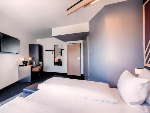 a bedroom with a white bed and a desk at B&B HOTEL München-Messe in Aschheim