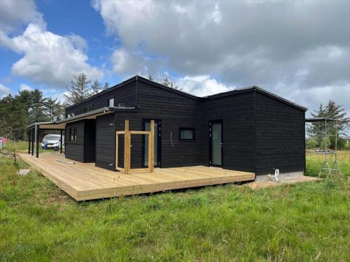 een zwart huis met een houten terras in een veld bij JB365-Fjerritslev-Hedestien-9 in Torup Strand